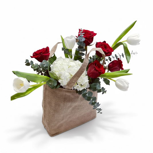 Floral arrangement with red roses, white hydrangeas, and tulips in a brown paper bag on a white background