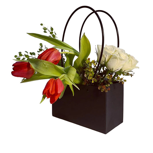 Floral arrangement in a black bag with red tulips and white roses on a white background