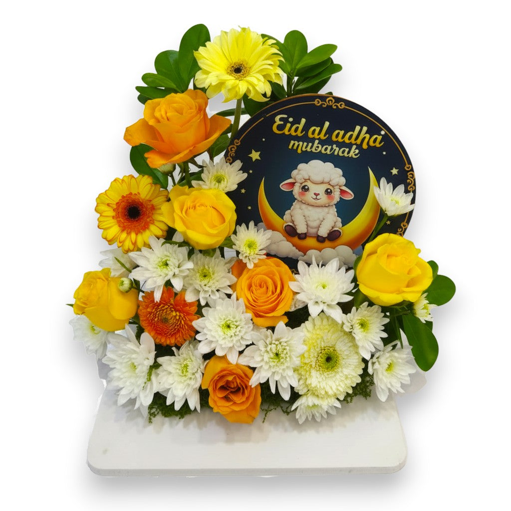 Floral arrangement with 'Eid al Adha mubarak' card featuring a sheep and crescent moon on a white background.