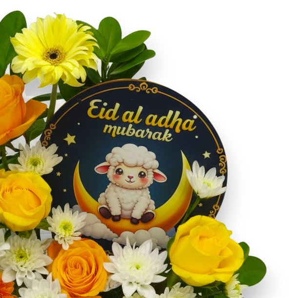 Floral arrangement with 'Eid al Adha mubarak' card featuring a sheep and crescent moon on a white background.