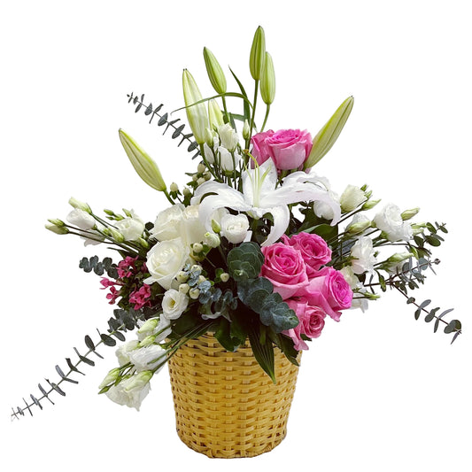 Floral arrangement with pink and white flowers in a yellow basket on a light gray background